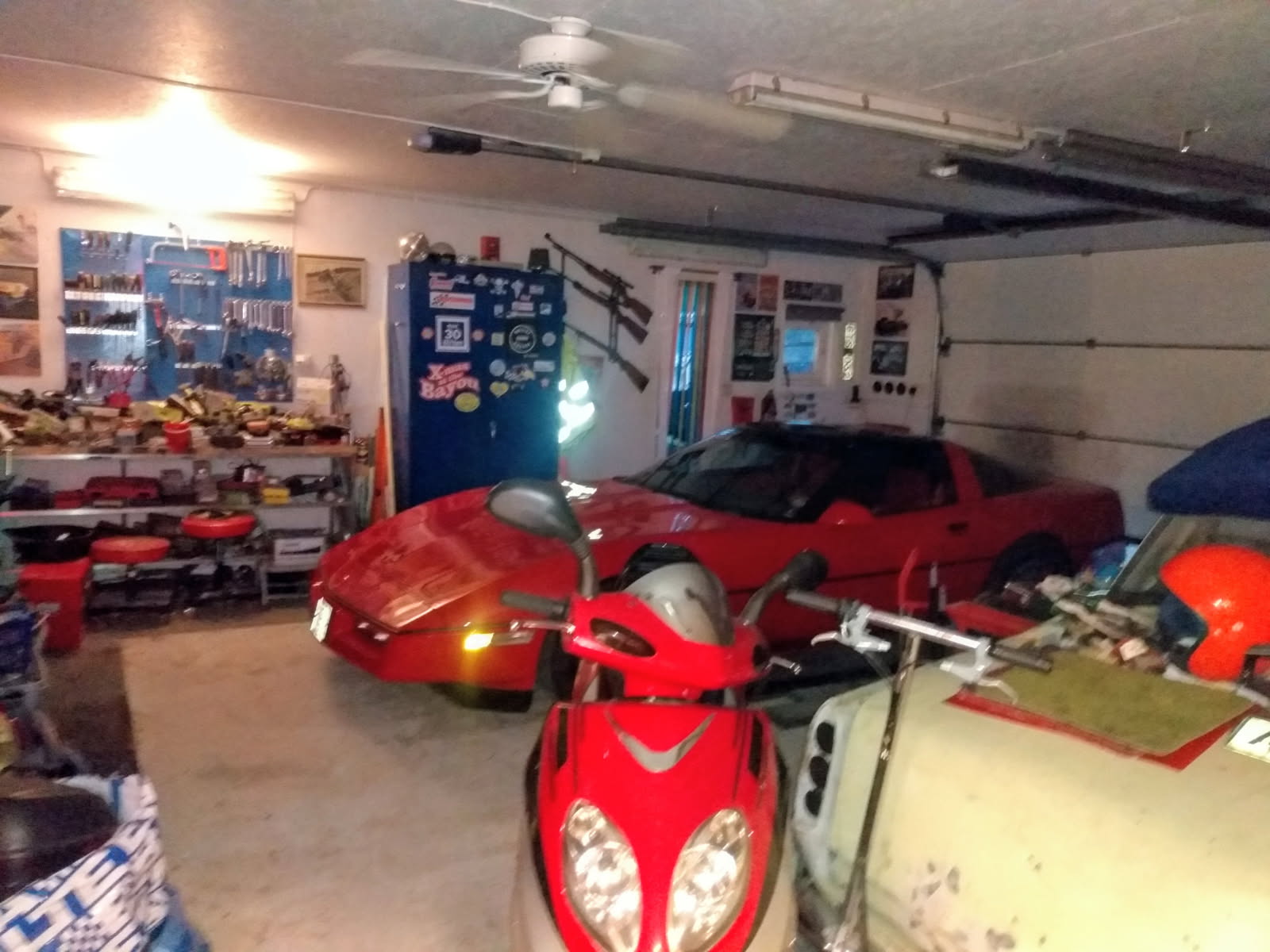 Röd Corvette parkerad inne i garaget bredvid moppe och prylar